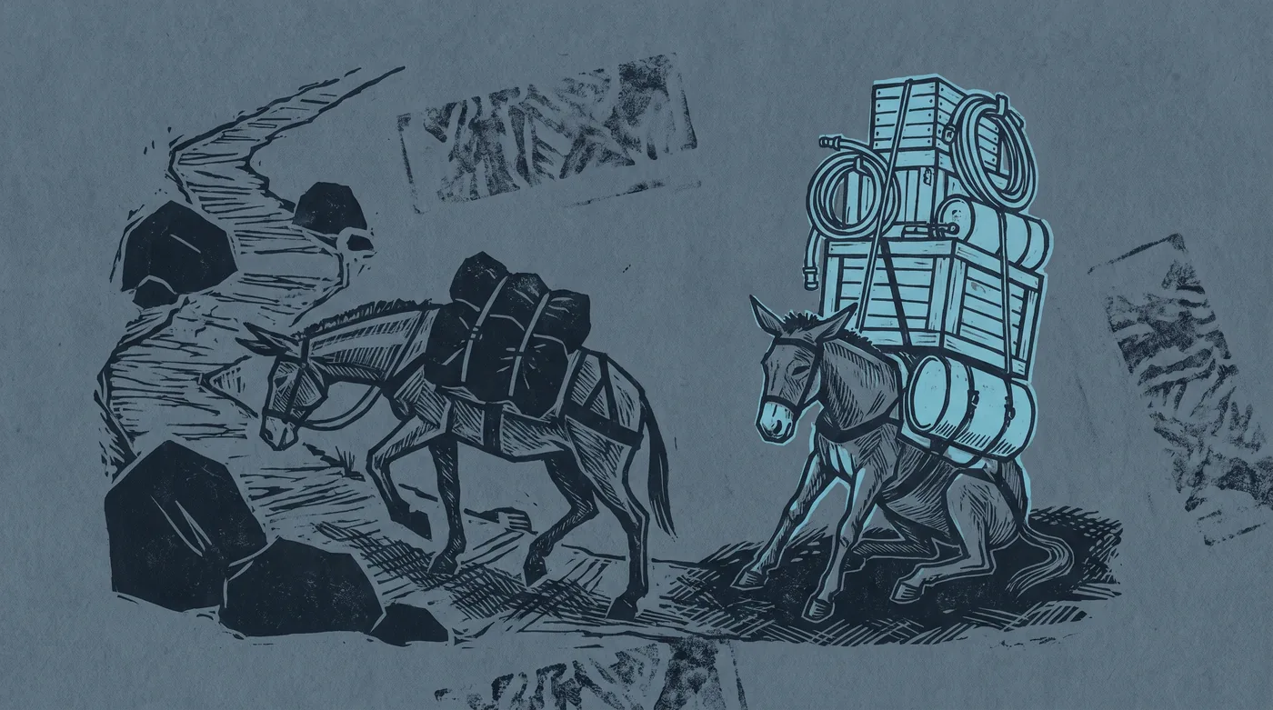 Two pack mules at the foot of a mountain trail. One strains under three bundles, head low. The other carries the same three bundles with a tall stack of crates, coils and canisters lashed on top, and has sat down in the dirt.